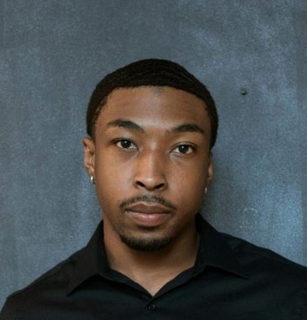 Portrait of a focused Black businessman in a black shirt holding a grid file against a textured wall.